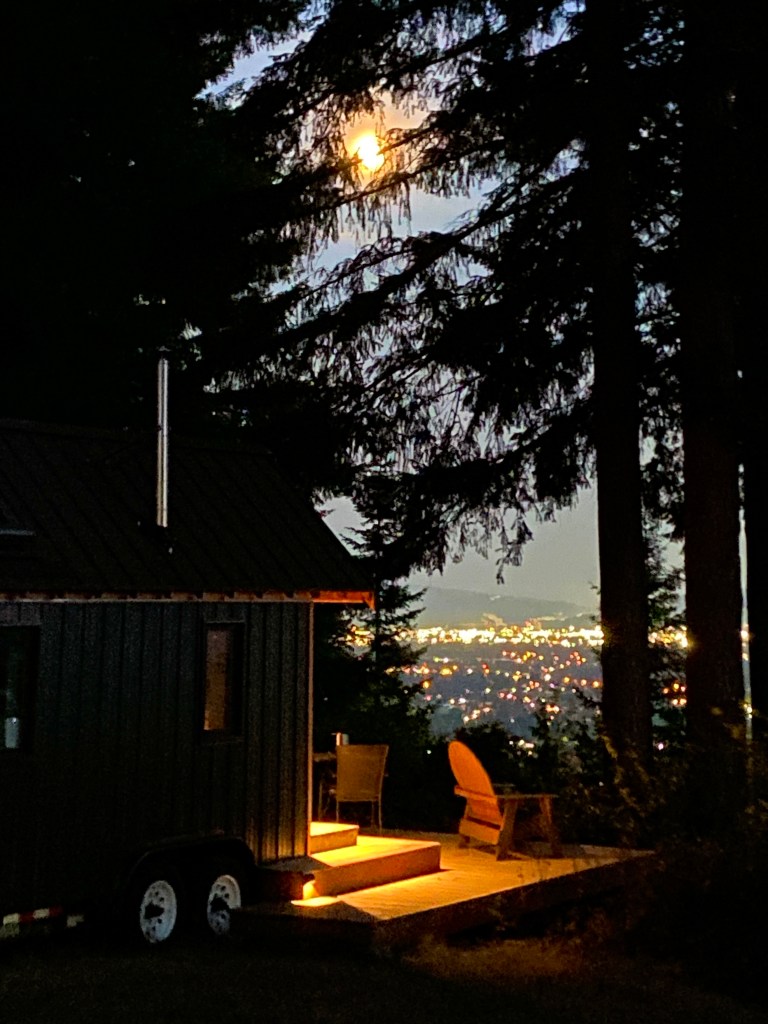 The Huckleberry Hut at night under a full moon with city lights below